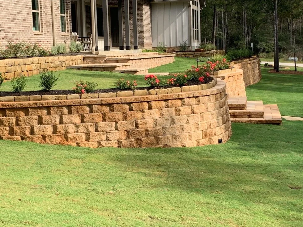 A custom multi-tiered stone retaining wall with integrated steps and landscaped flower beds, expertly designed and installed by Results Tree & Landscape Inc. in Magnolia, Texas.