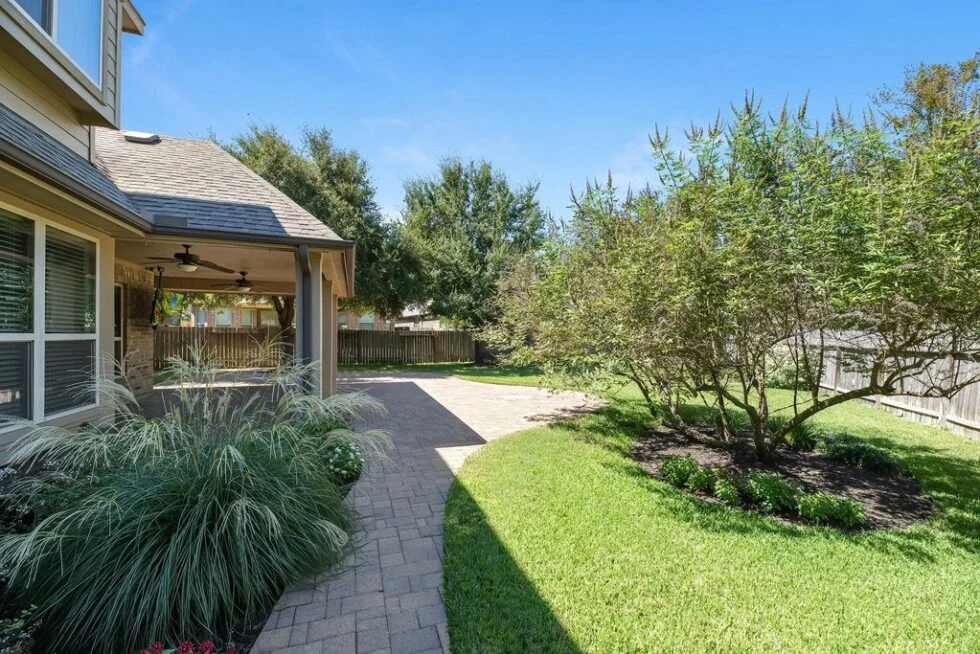 Professionally landscaped backyard in Magnolia, TX, featuring a stone paver walkway, manicured lawn, and ornamental trees designed by Results Tree and Landscape.
