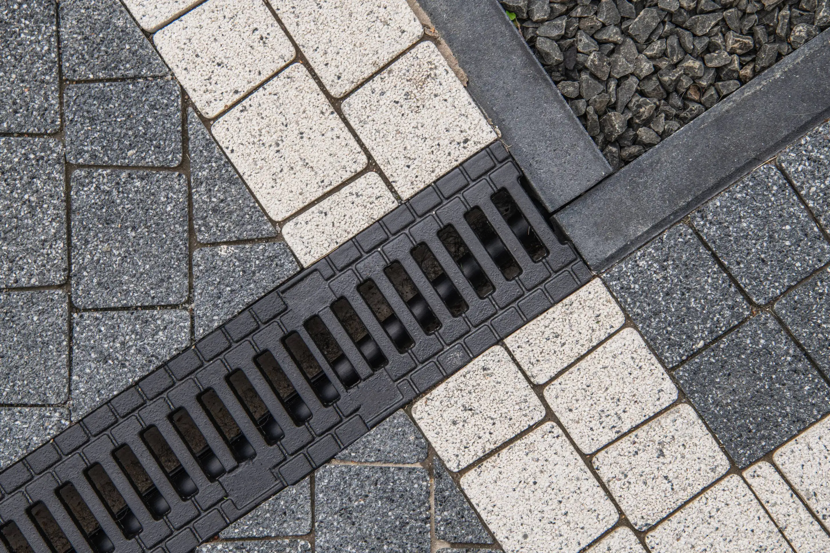 A linear channel drain system installed within a custom stone paver surface to control runoff, expertly engineered by Results Tree & Landscape Inc. in Magnolia, Texas.
