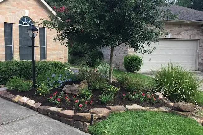 Residential front yard landscaping featuring natural stone borders, fresh mulch, and colorful flower bed installation by Results Tree & Landscape Inc. in Magnolia, TX.