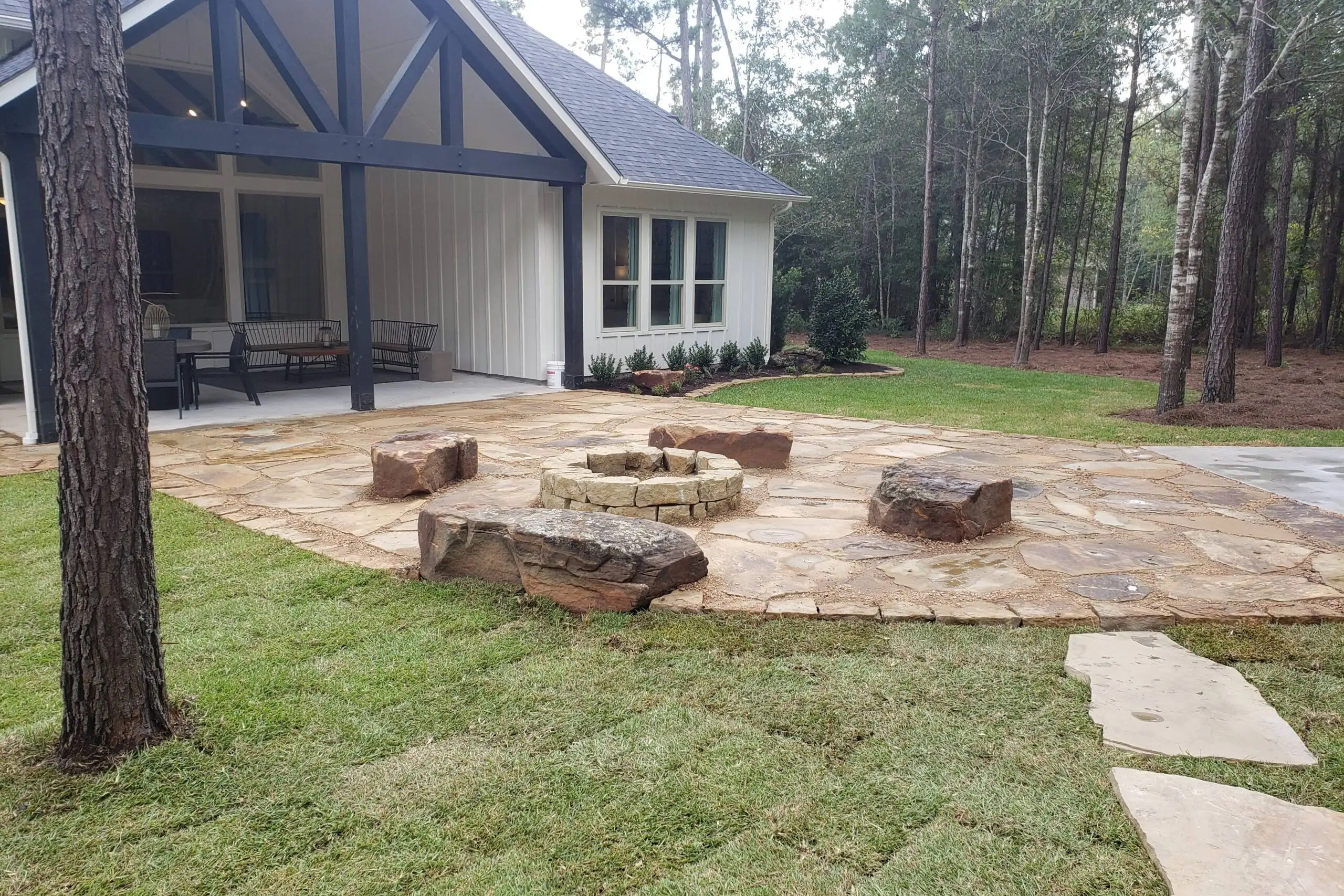 Backyard hardscape design featuring a flagstone patio, custom fire pit, and natural stone seating blocks installed by Results Tree & Landscape Inc.