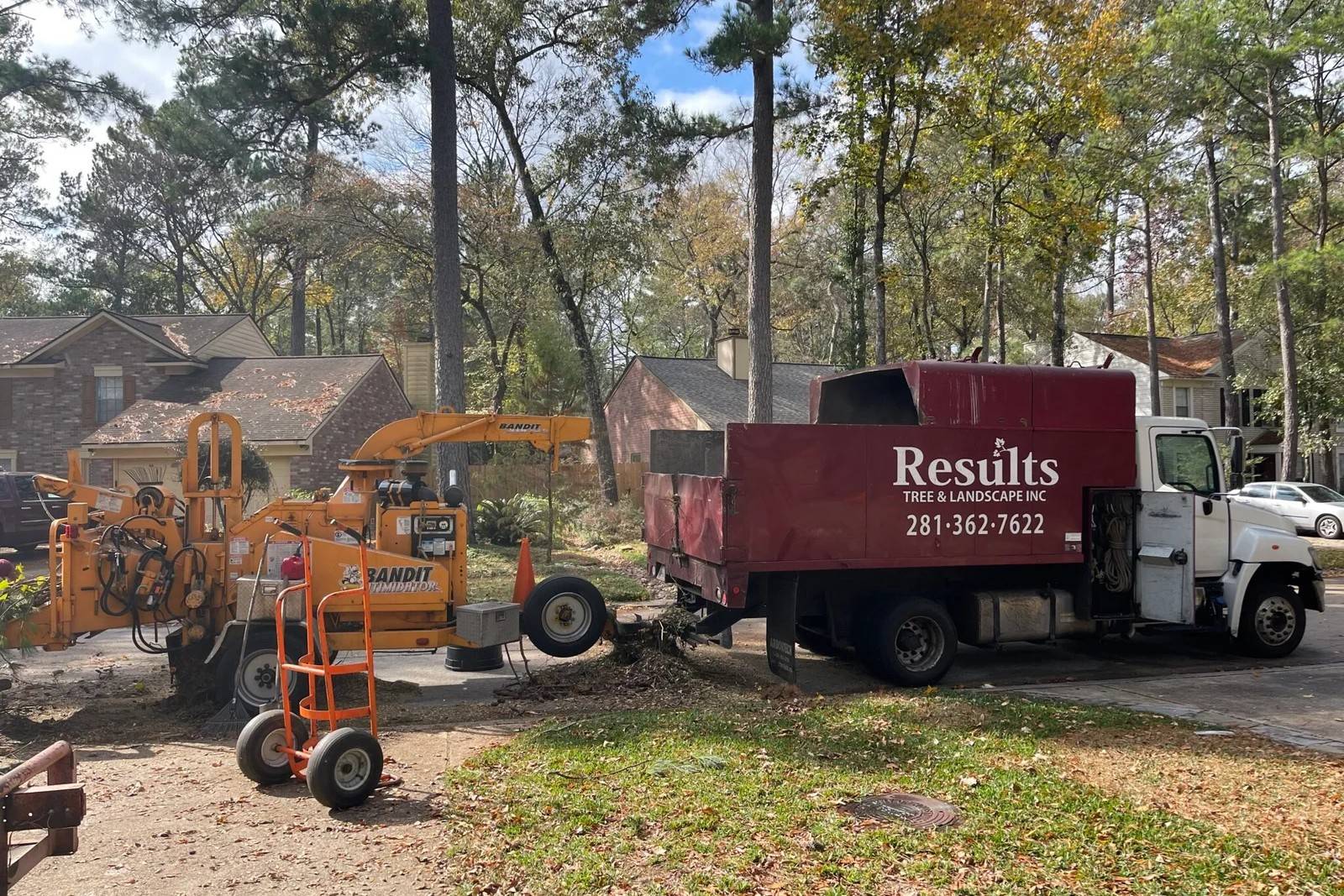Results Tree & Landscape Inc. branded red dump truck and wood chipper performing tree removal and trimming services at a residential property.