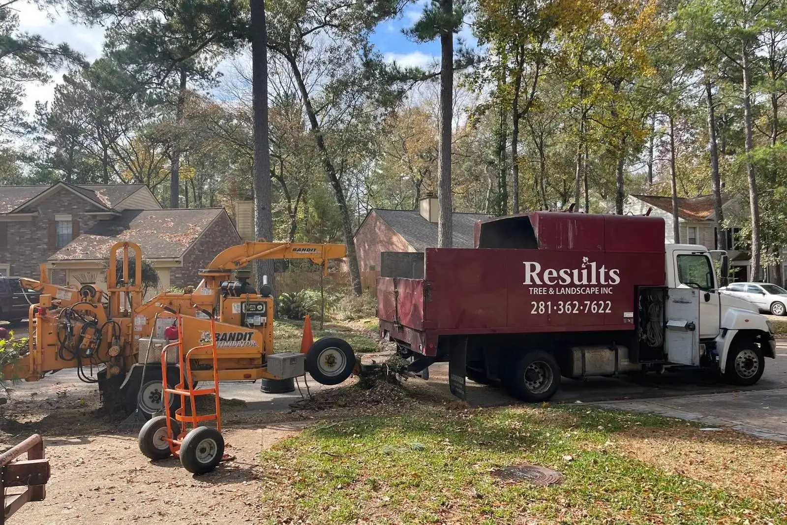 Results Tree & Landscape Inc. branded red dump truck and wood chipper performing tree removal and trimming services at a residential property.