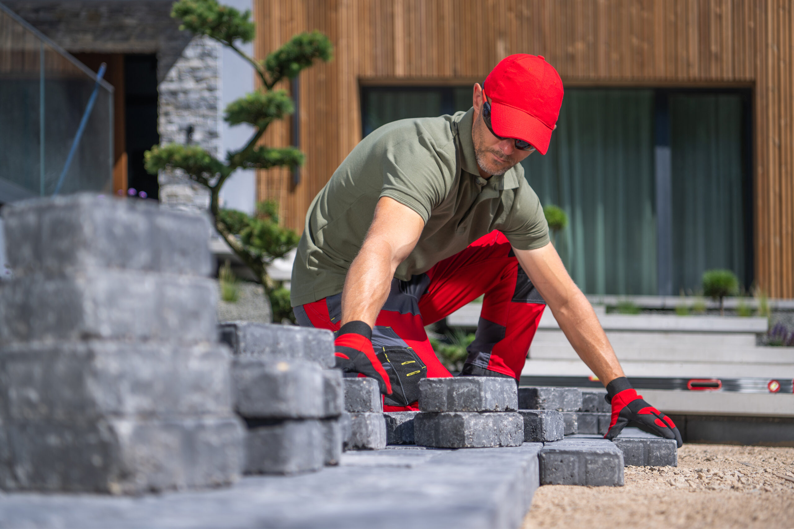 Worker Laying Stone Pavers in Modern Garden During Bright Daytime Patio Installation & Outdoor Patio Builder<br />